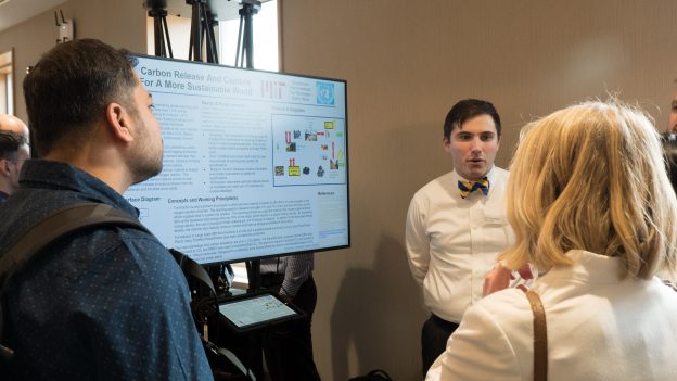 James Pennington, SDM '18, discusses his team's poster at the Technology Showcase with fellow students.