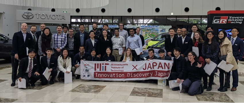 Students stand in a showroom at the Toyota Kaikan Museum holding the MIT IDJ banner.