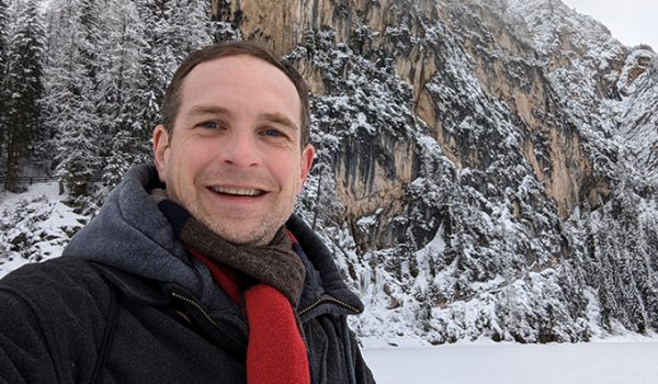 Chad Holmes stands in front of a snowy mountain peak.