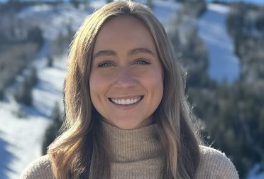 Headshot of Caroline Vincent, a blonde woman wearing an oatmeal-colored turtleneck. In the background is a snowy hill with evergreen trees.