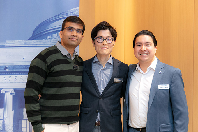 Three men stand with arms around each other, smiling at the camera.