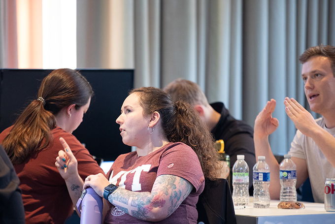 One woman wearing an MIT tee shirt describes something to another woman, who is facing away from her.