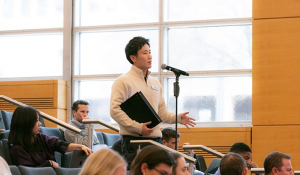 A student stands in an auditorium at a microphone, in the middle of asking a question.