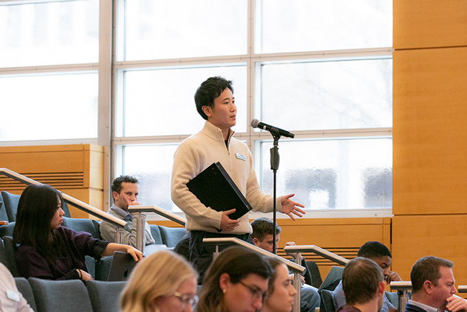 A student stands in an auditorium at a microphone, in the middle of asking a question.