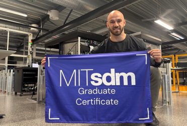 Luc Vernery holding an MITsdm Graduate Certificate banner, kneeling in a warehouse