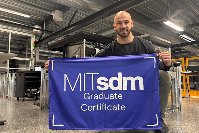 Luc Vernery holding an MITsdm Graduate Certificate banner, kneeling in a warehouse