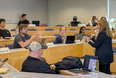 Prof. Donna Rhodes and a student discussing something, in a classroom with several tiers of desks. Other students look on.