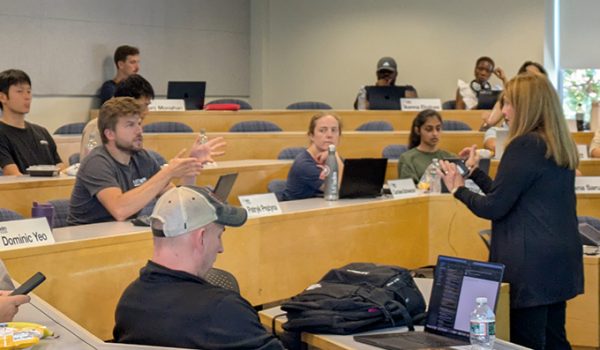 Prof. Donna Rhodes and a student discussing something, in a classroom with several tiers of desks. Other students look on.