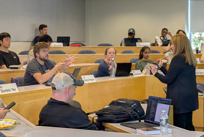 Prof. Donna Rhodes and a student discussing something, in a classroom with several tiers of desks. Other students look on.
