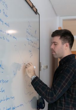 A student standing at a whiteboard, writing on it with a marker.