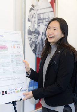 A student stands beside a scientific poster, smiling at someone outside the picture's frame.