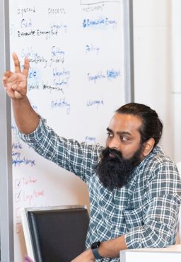A student raising his hand while sitting in front of a whiteboard full of notes