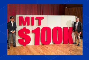 Hiro Ogasawara and Rowell Castro stand on either side of a large three-dimensional sign for the MIT $100K Challenge.