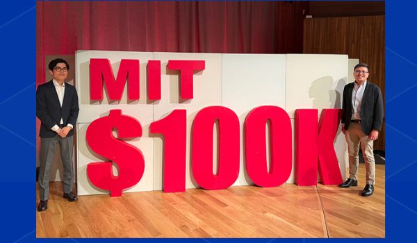 Hiro Ogasawara and Rowell Castro stand on either side of a large three-dimensional sign for the MIT $100K Challenge.