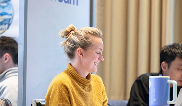 A woman in a yellow sweater sitting in a classroom laughs.