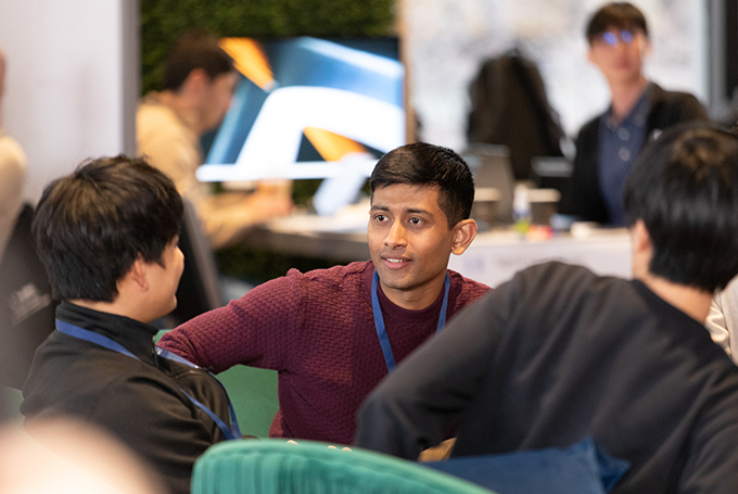 Three students sitting on couches, two facing away from the camera and one facing the camera, engaged in conversation.