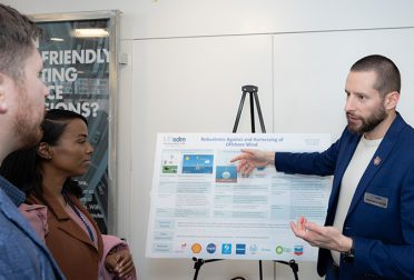 One student explains a scientific poster to two other students.