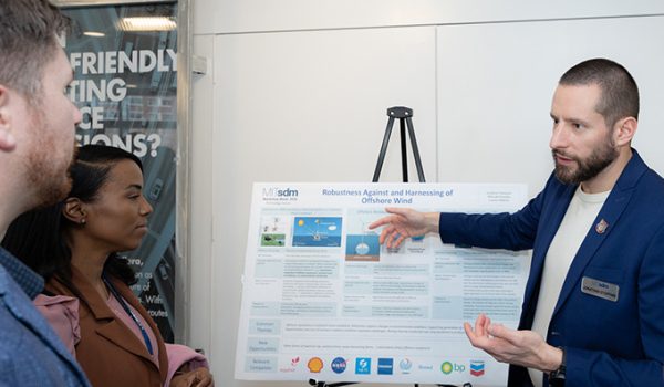 One student explains a scientific poster to two other students.