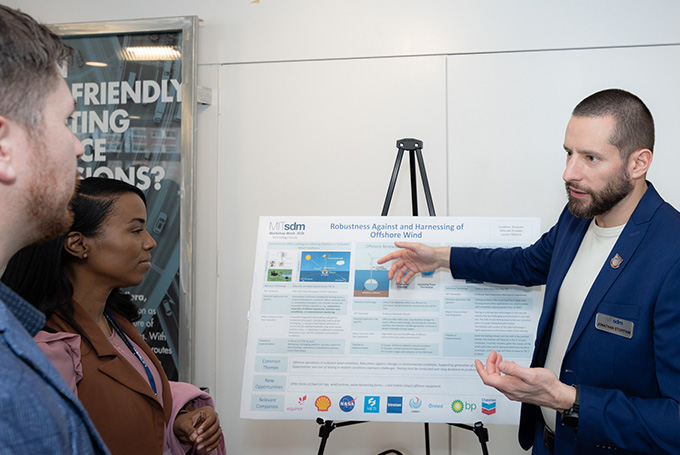 One student explains a scientific poster to two other students.