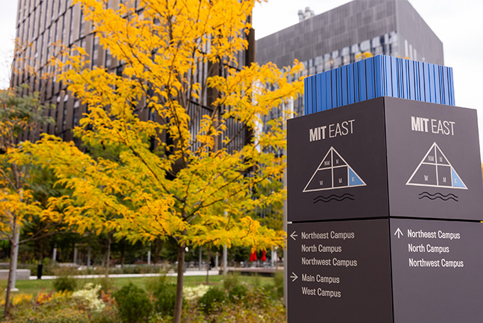 A tree with yellow fall foliage behind a wayfinding sign on the MIT campus.