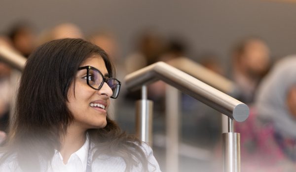 A student in a lecture hall looks up and away from the camera, smiling.