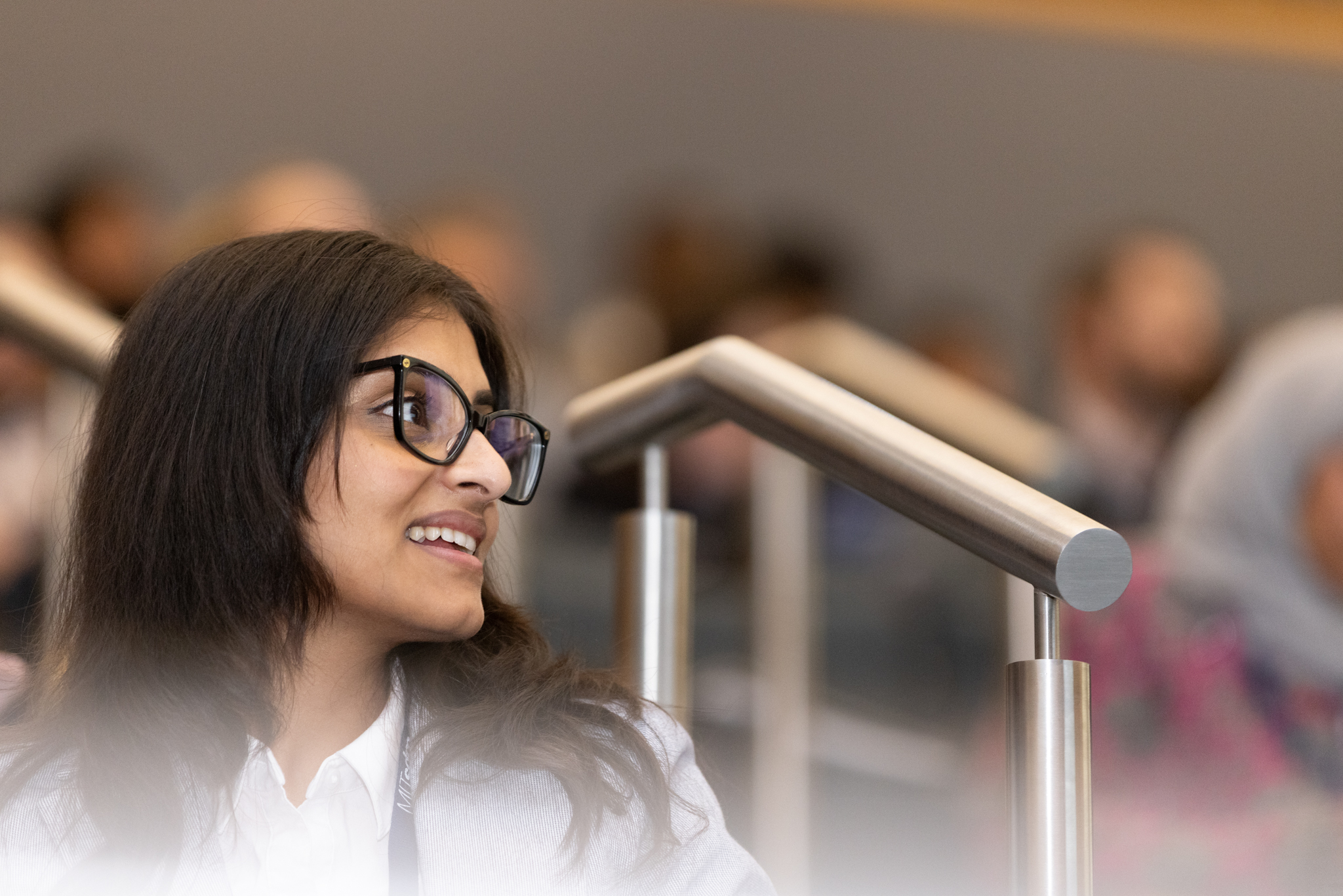 A student in a lecture hall looks up and away from the camera, smiling.