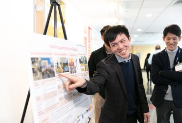 A smiling student points something out on a scientific poster.