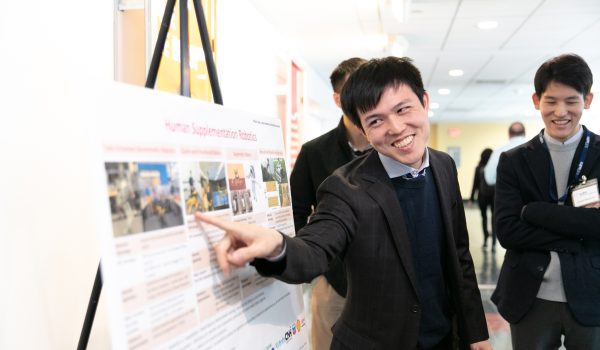 A smiling student points something out on a scientific poster.