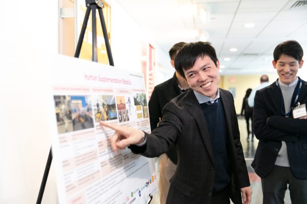 A smiling student points something out on a scientific poster.